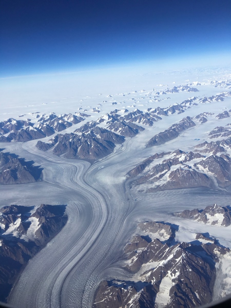 View of glaciers flowing past mountains from plane flying over Greenland