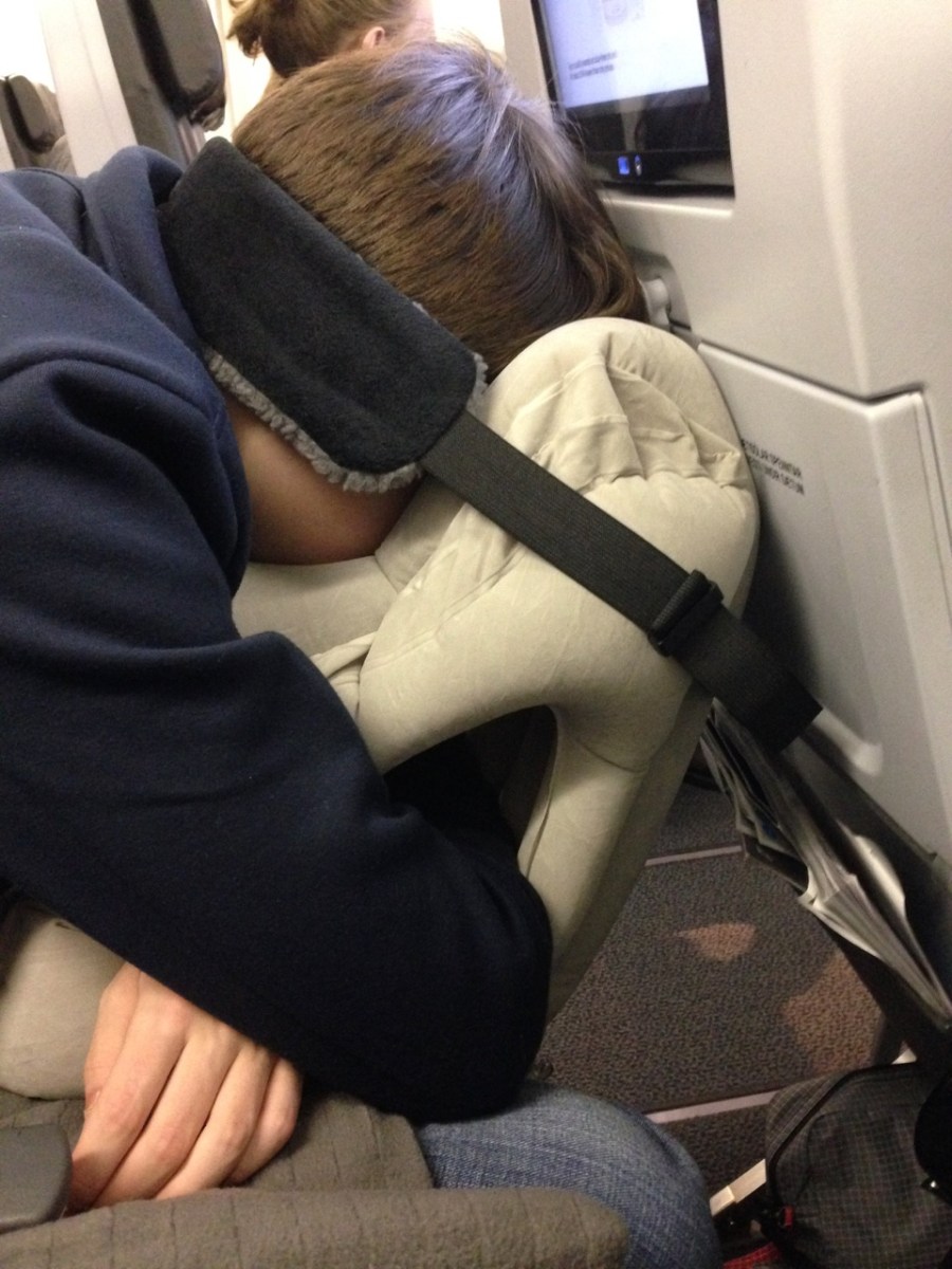 Young man sleeping on plane leaning forward wiht face buried in inflatable pillow