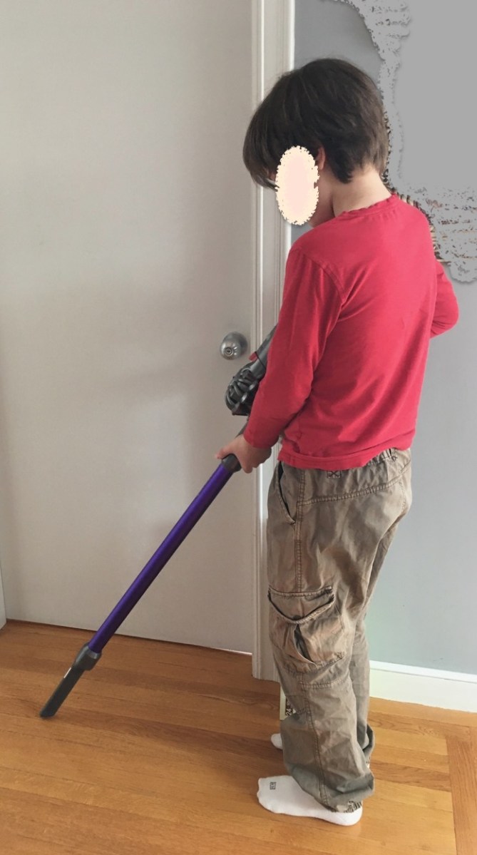 Boy holding stick vacuum as if cleaning the floor