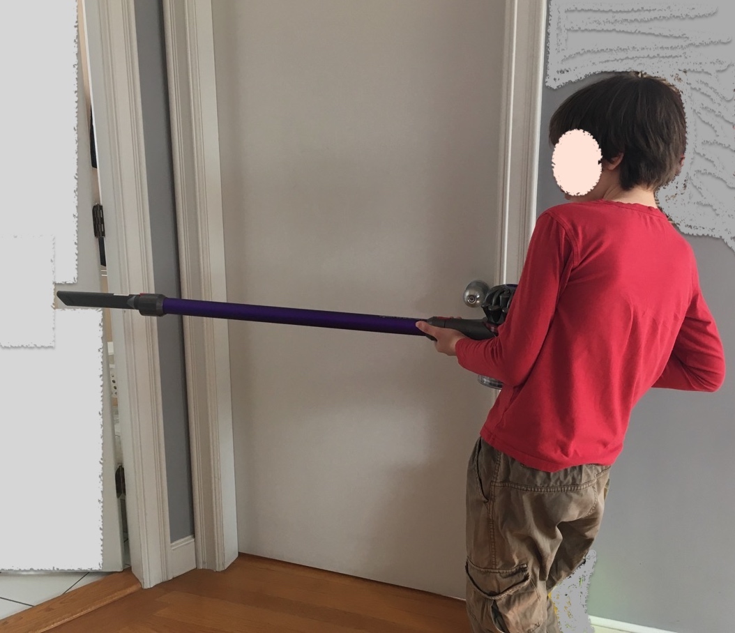 Boy holding stick vacuum like a machine gun