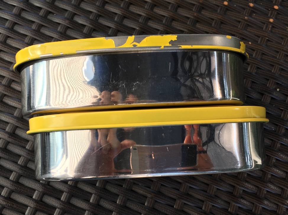 side view of two 10 year old LunchBots Pico stainless containers, 1 with new lid