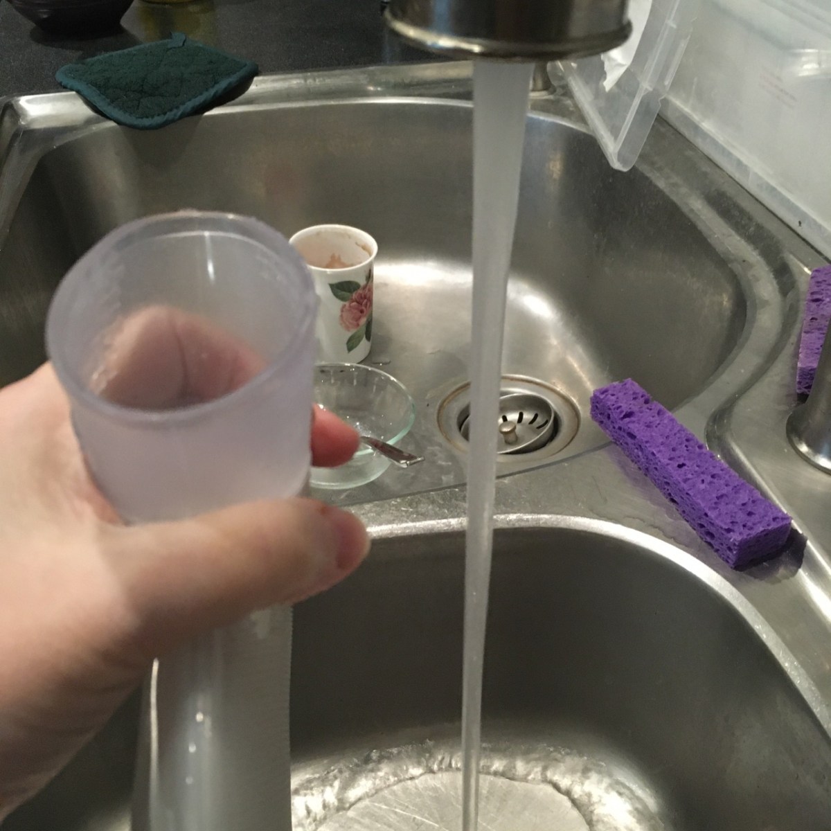 water running to fill hot water bottle with dirty dishes visible in double sink basin