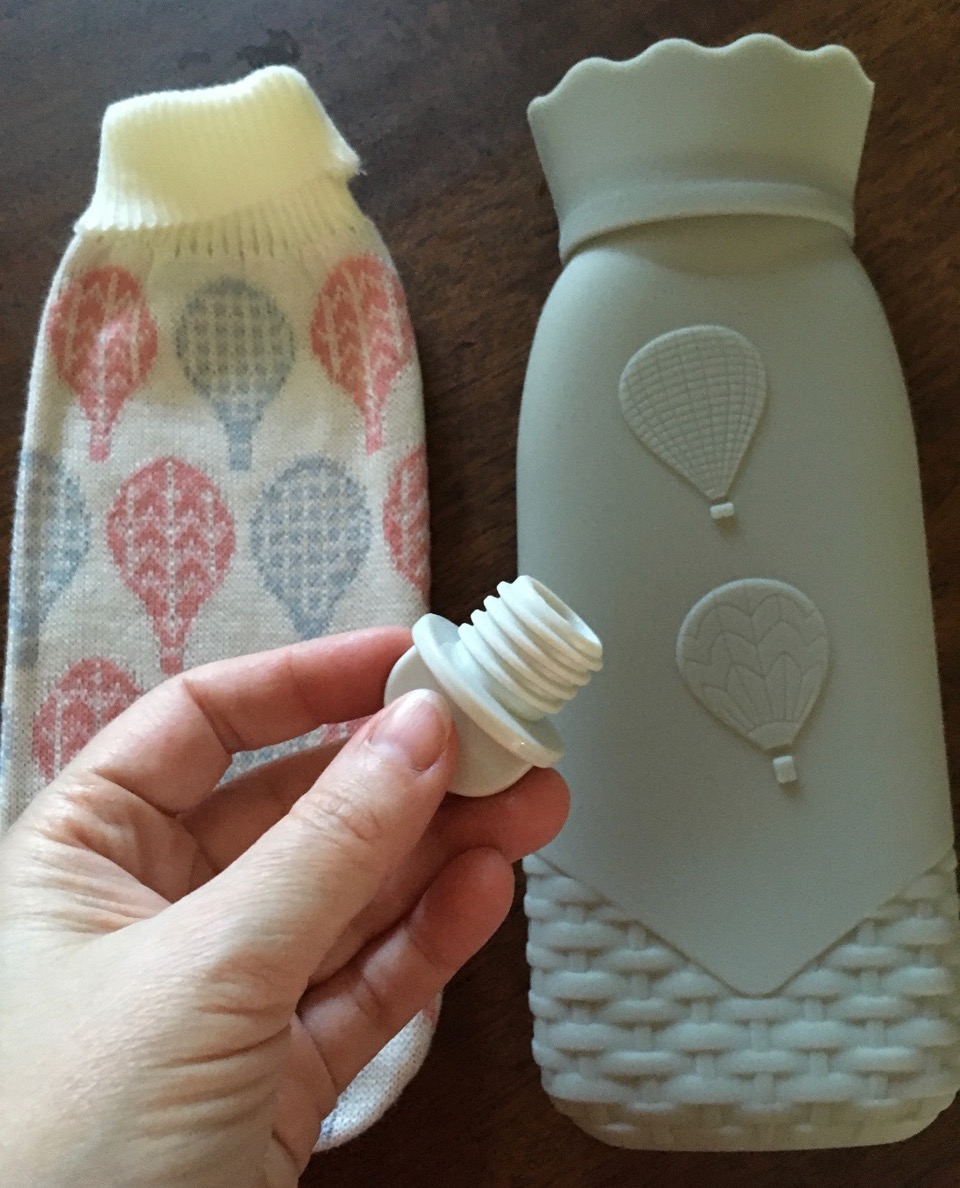 Grey silicone hot water bottle shown with acrylic knit cover and its plastic stopper