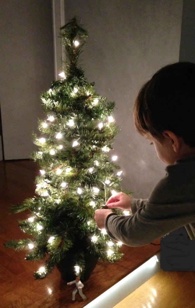 child hangs ornament on small Christmas tree