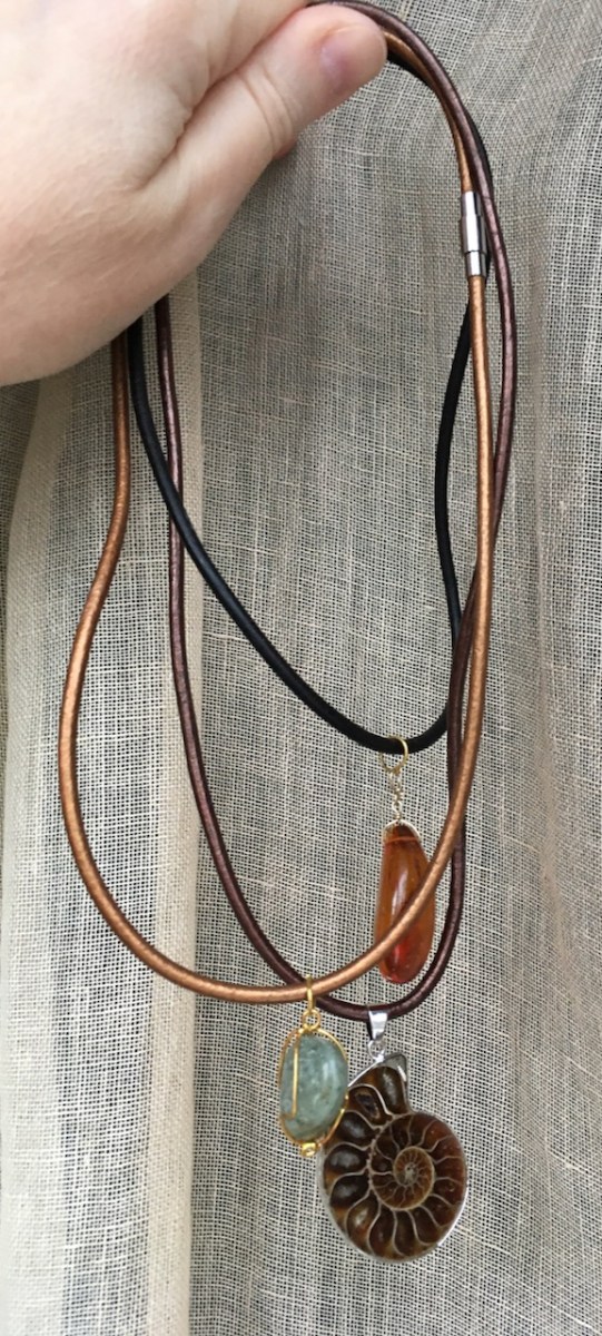 Pendant necklaces: amber bead on black cord, ammonite fossil pendant on brown cord, blue stone on bronze cord