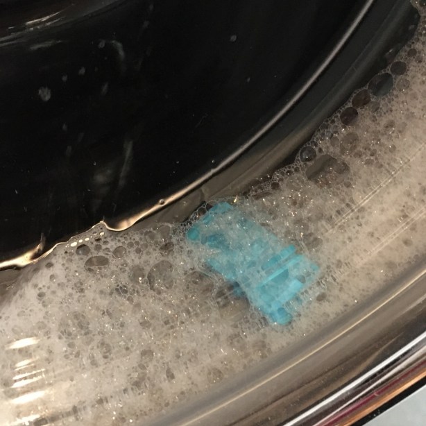 Bright blue plastic USB drive housing in pile of suds viewed through washing machine door