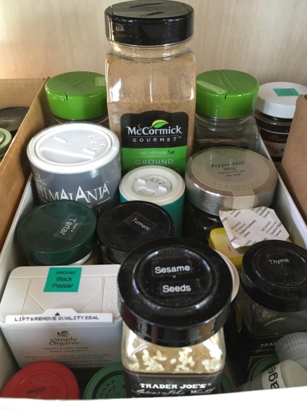 Costco sized bulk shakers of spices in open topped box with various jars and tins including short bottles almost hidden