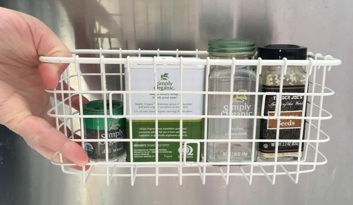 hand holding a small white wire basket containing four assorted spice jars and tins