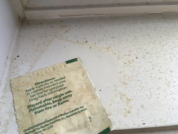 Topical wipe covered in pollen on pollen-coated windowsill near outline from the shifted packet