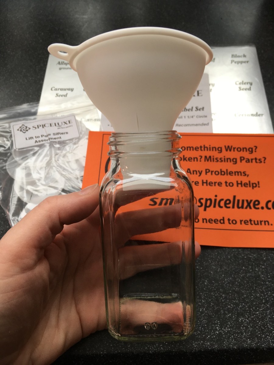 White funnel in spice bottle with shaker lids and silver labels in background