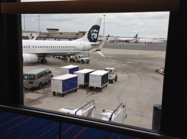 Tail of Alaska plane visible on tarmac through airport terminal window