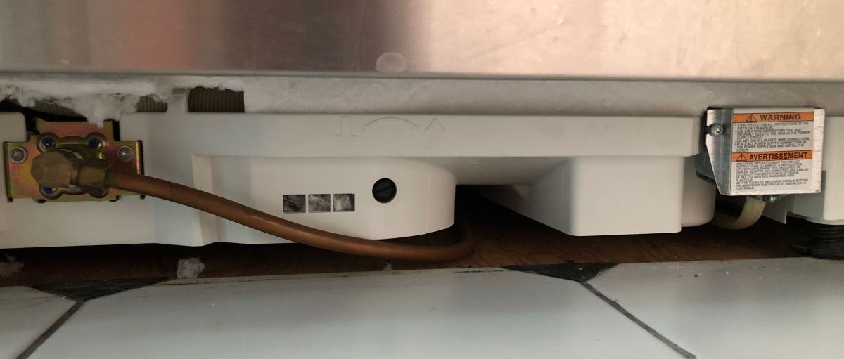 kickplate removed from stainless steel dishwasher showing hardwiring and soldered copper pipe instead of flexible tubing