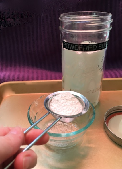sifting powdered sugar into small bowl with handheld stainless sieve