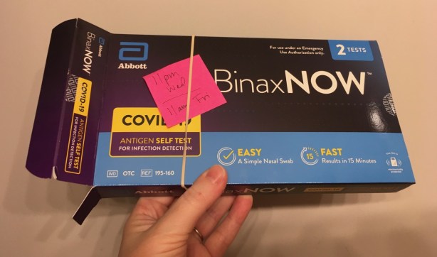 Open COVID-19 test box with post it note reminder to test twice, 72 hours apart