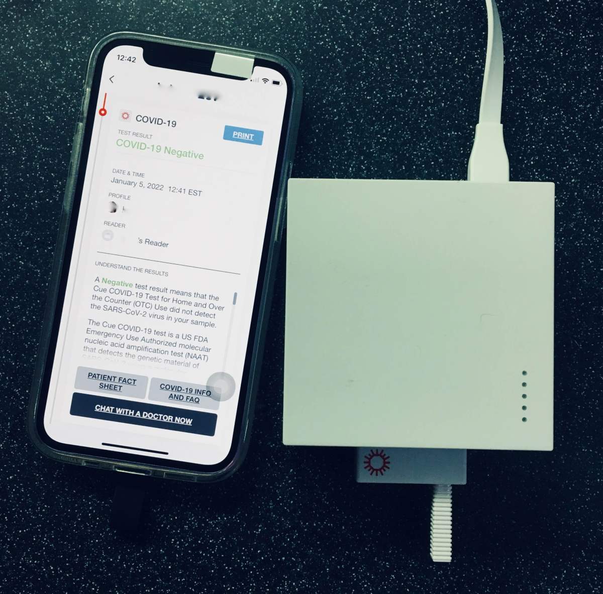 iPhone running Cue App next to Reader device with COVID-19 test plugged in