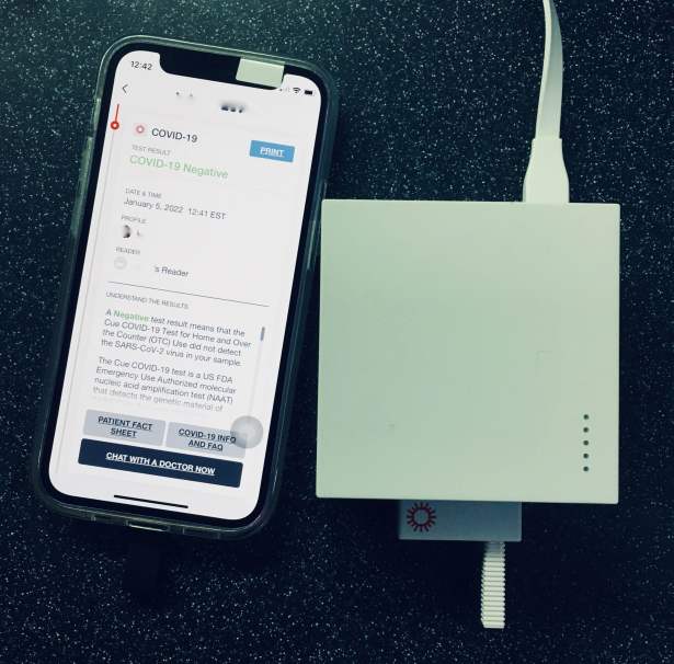iPhone running Cue App next to Reader device with COVID-19 test plugged in