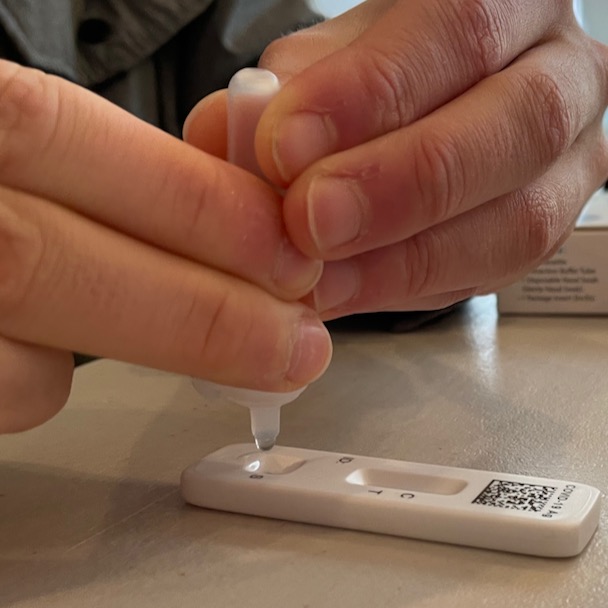 Hands squeezing to dispense drop of liquid for COVID test onto cartridge
