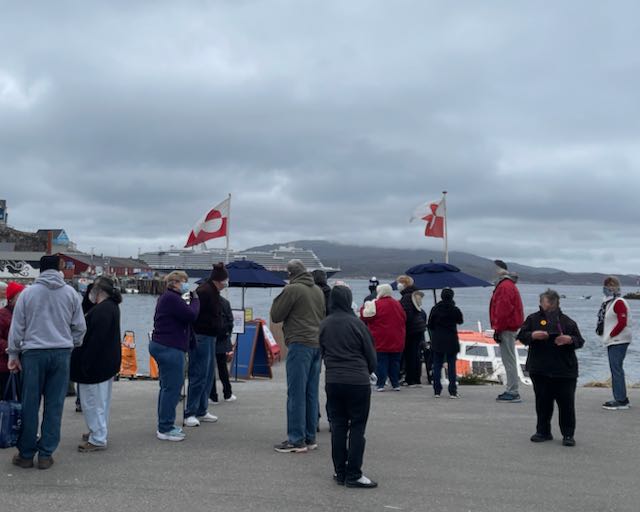 Two folding umbrellas under Greenland flags show where to find ship's representatives on shore