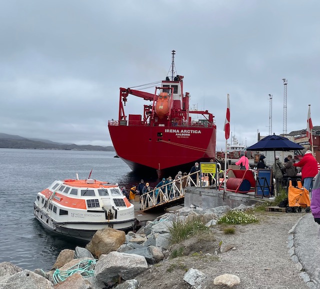 A working vessel looms over ship's tender disgorging cruise passengers up ramp