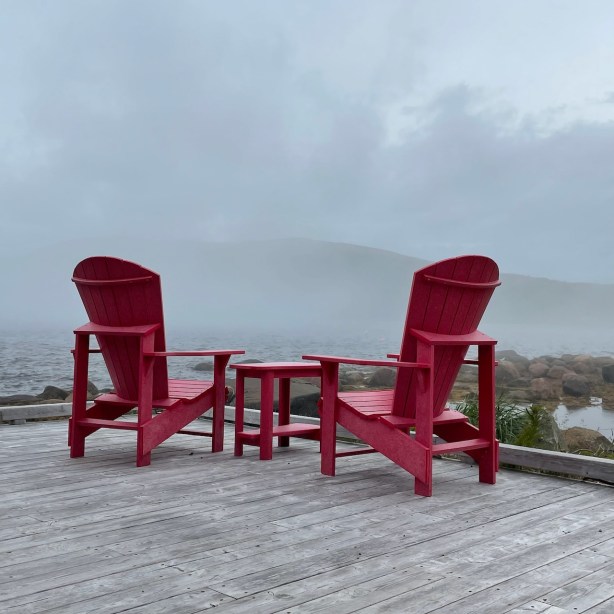 Pair of Adirondack chairs at the end of a jetty facing foggy sea