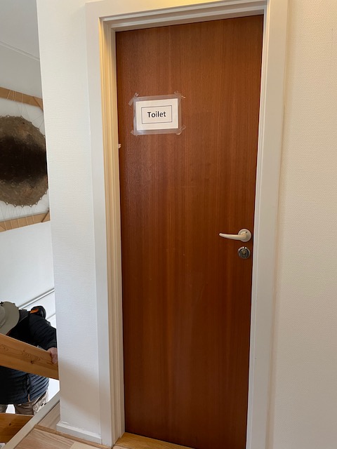 At the top of the stairs, a simple Toilet sign taped on single user bathroom door