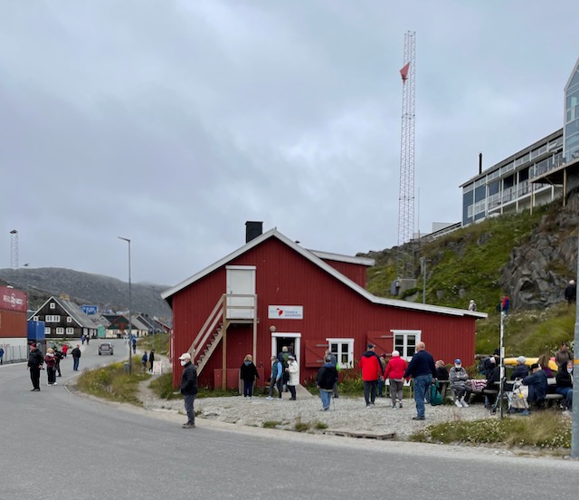 View across paved road of red building welcoming visitors to Qaqortoq