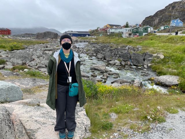 Me, in rian gear, in front of lovely view of creek running over rocks through middle of town