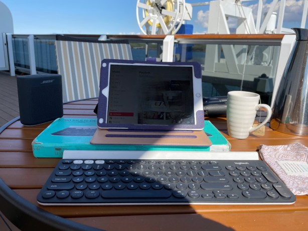 Set up to work on balcony with iPad, bluetooth keyboard, cup of tea and HAL's speaker and binoculars visible behind my tablet