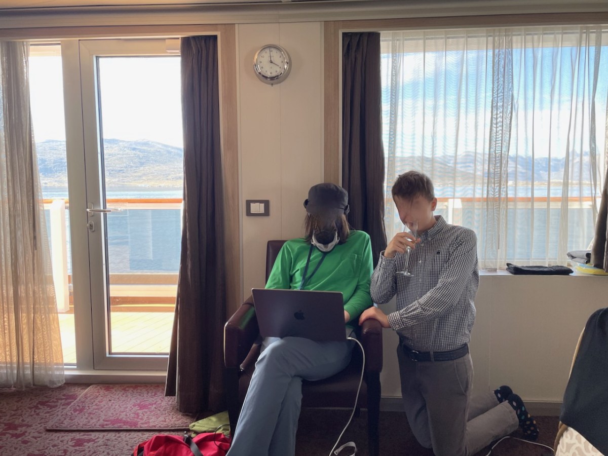 Two teens sitting by balcony door looking at laptop, wide windowsill beside them with room to set down a glass