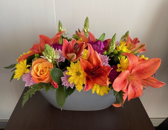Holland America line florist bouquet by request in wide bowl with orange, yellow and purple blooms