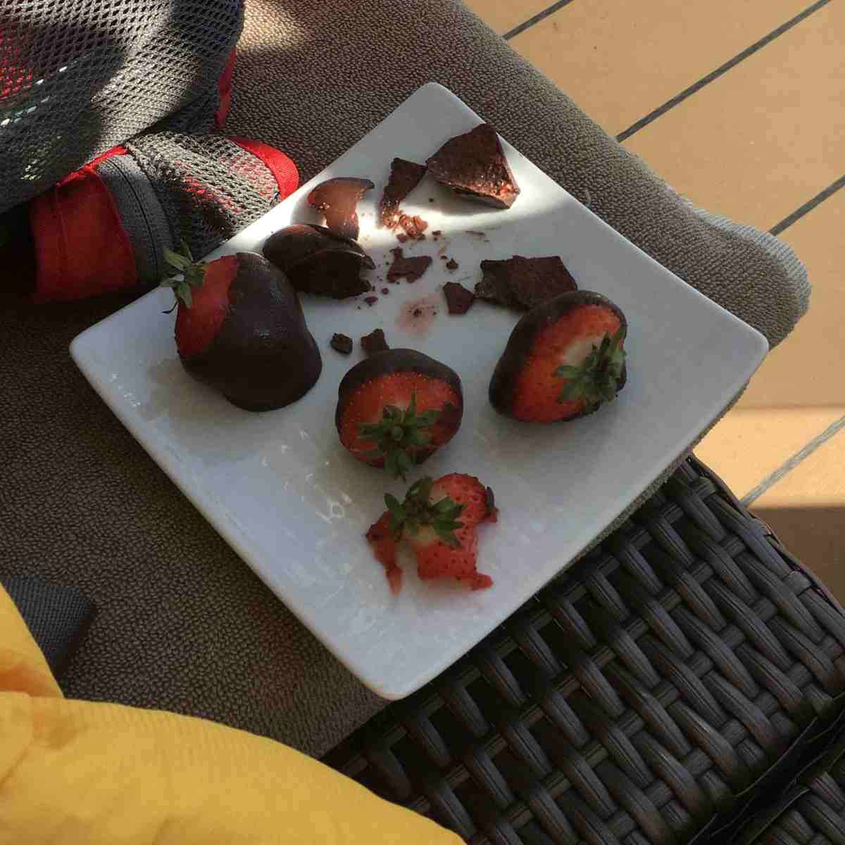 Plate of partially consumed chocolate dipped strawberries on lounge chair