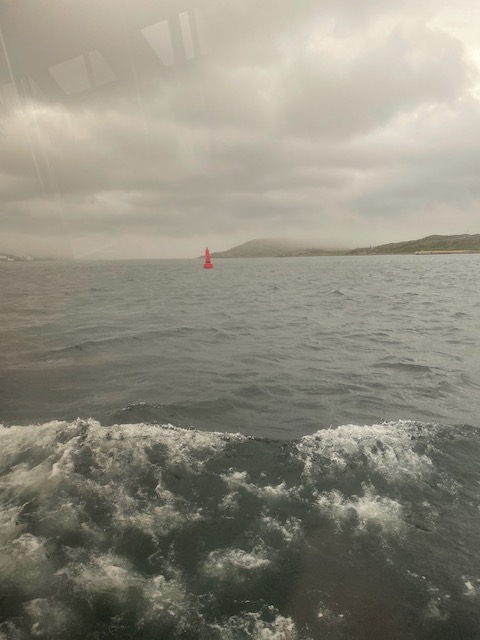 View of buoy through tender window showing white capped waves under foggy sky