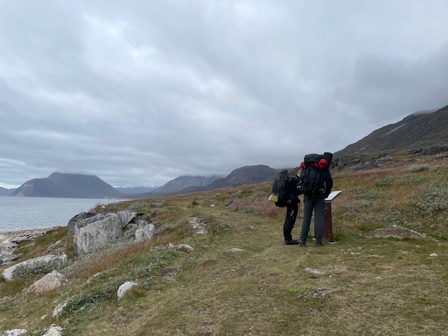 A pair of backpackers view the metal sign, roughly 12 x 24 inches in size