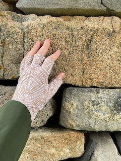 Lady's hand in patterned, fingerless sun protection glove on golden stone in stacked wall